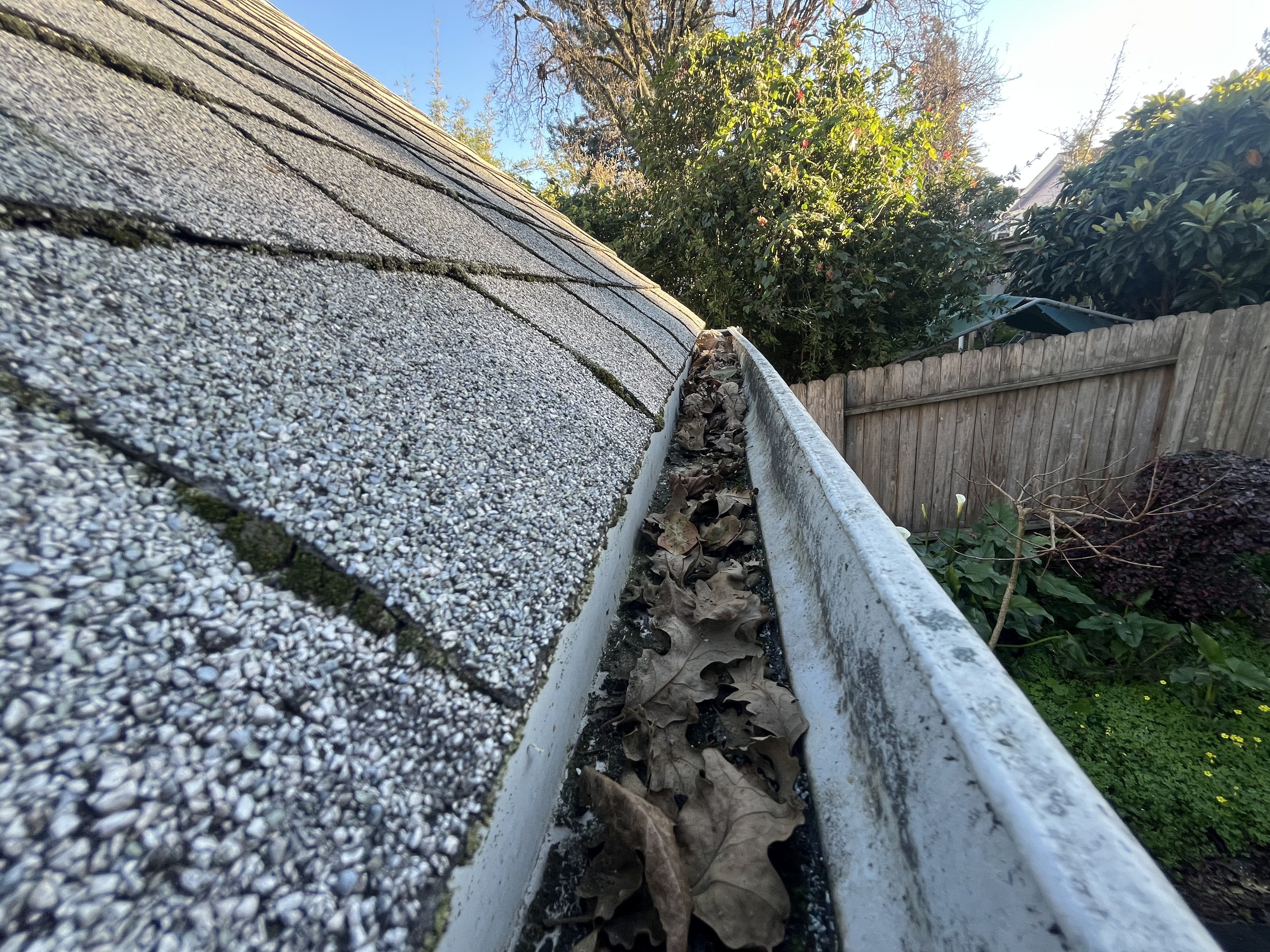 Vertical gray-brown overflow streaks running down the front face of a white painted steel gutter — tiger stripes from repeated overflow at capacity