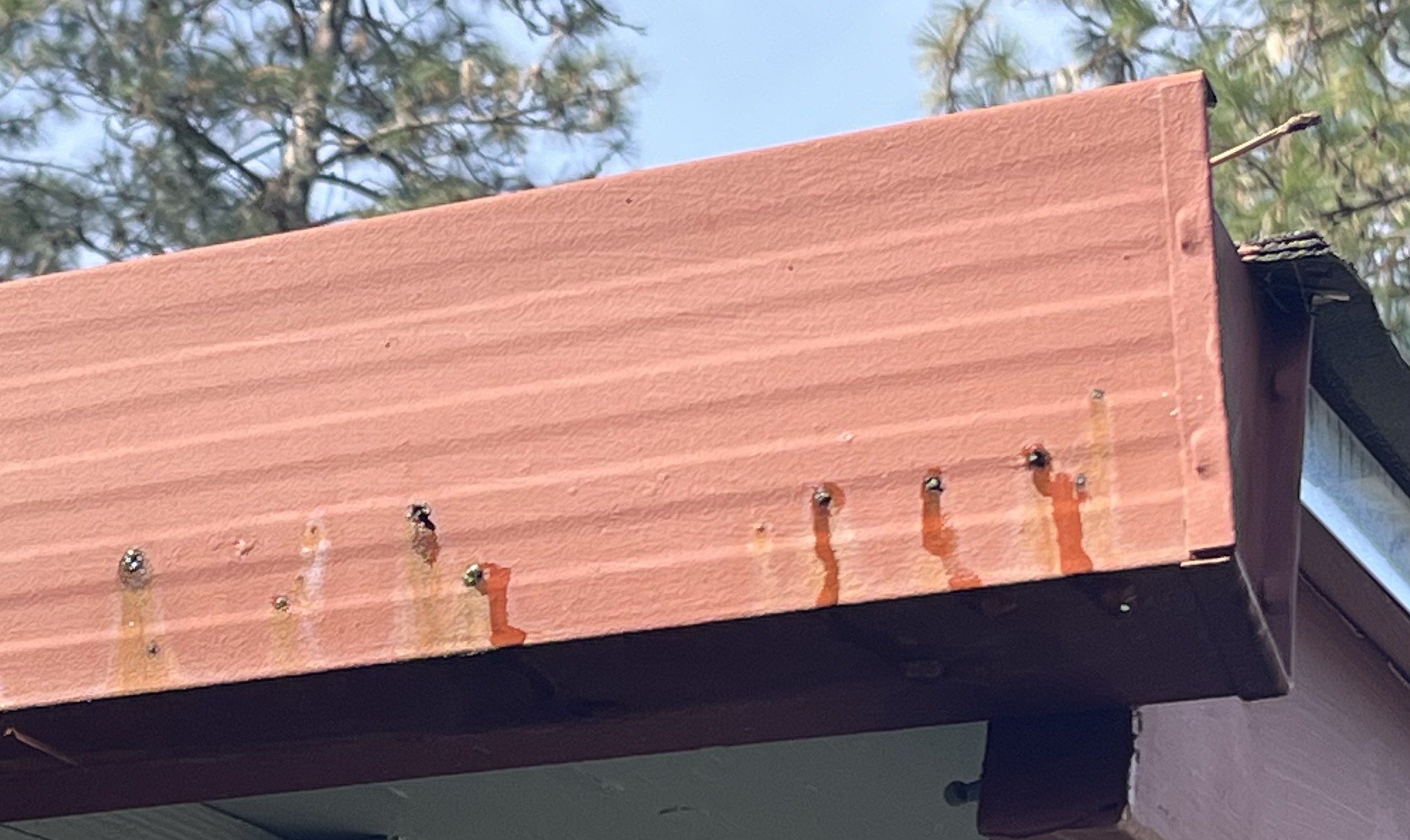 Orange rust streaks running down the front face of a salmon-painted steel gutter from every mounting screw — fastener corrosion, not gutter failure