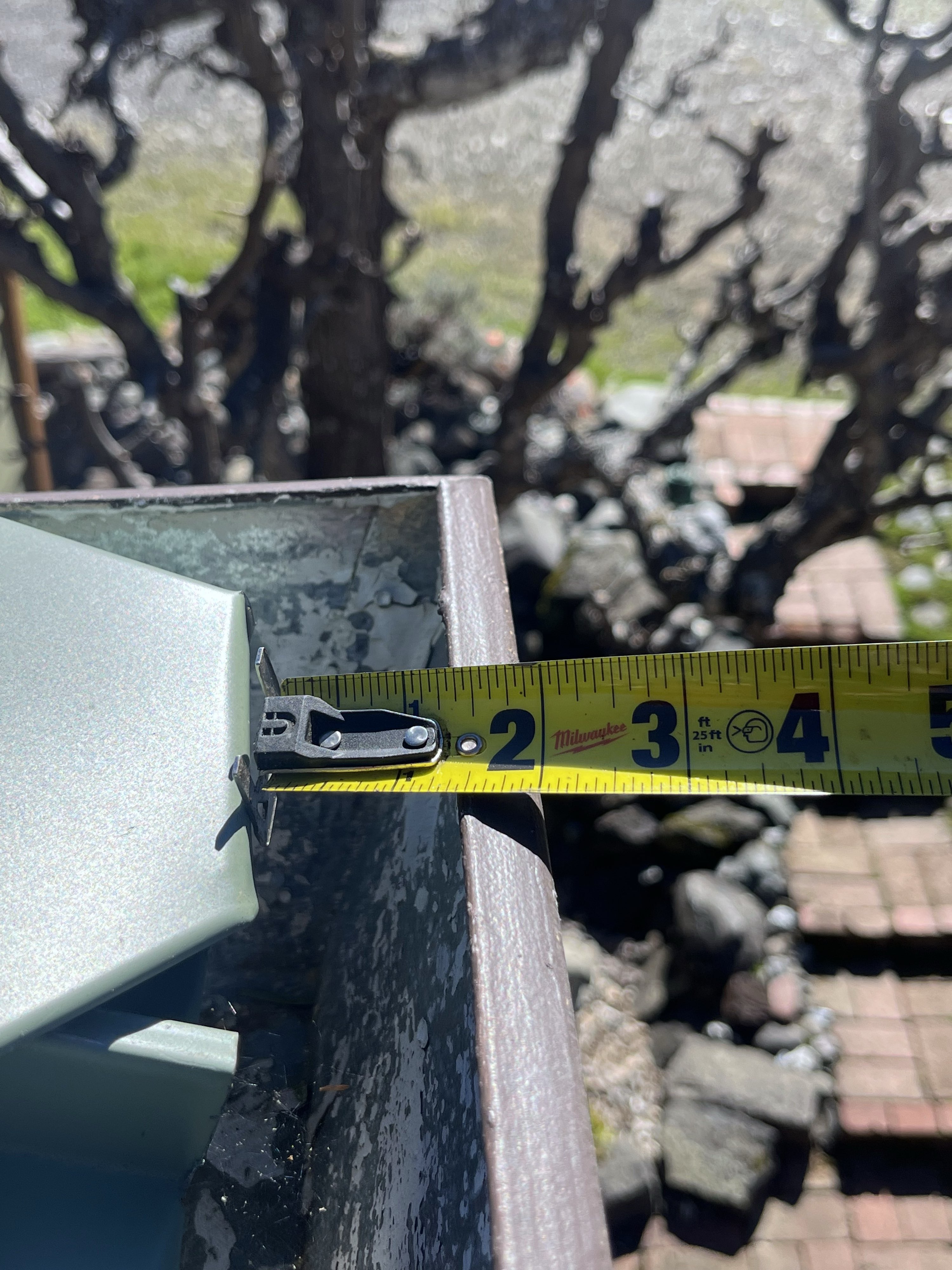 Milwaukee tape measure laid across a K-style aluminum gutter opening, reading approximately 3 inches — narrow-profile access constraint where standard guard panels do not fit
